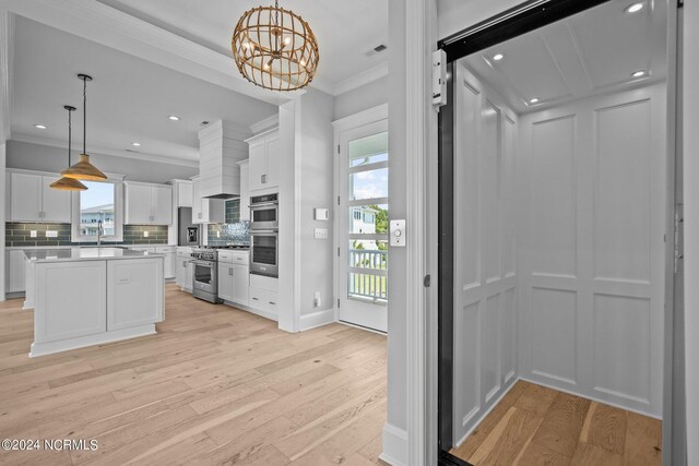 kitchen featuring stainless steel appliances, decorative light fixtures, white cabinetry, and light hardwood / wood-style floors