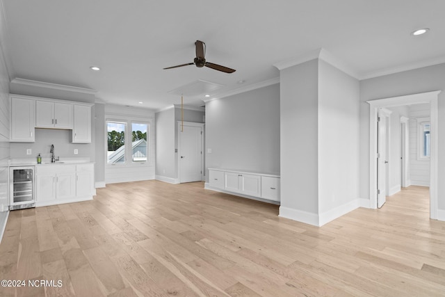 unfurnished living room with crown molding, wet bar, beverage cooler, ceiling fan, and light hardwood / wood-style floors