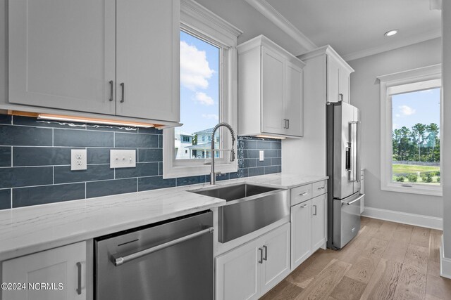 kitchen with stainless steel appliances, sink, light stone countertops, and light hardwood / wood-style floors