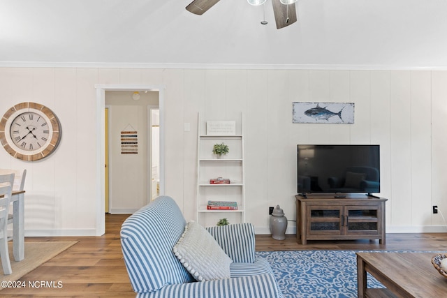 living room featuring ceiling fan, built in shelves, wood walls, ornamental molding, and hardwood / wood-style floors