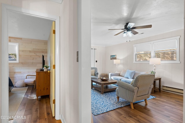 living room with a baseboard heating unit, ceiling fan, hardwood / wood-style floors, and wooden walls