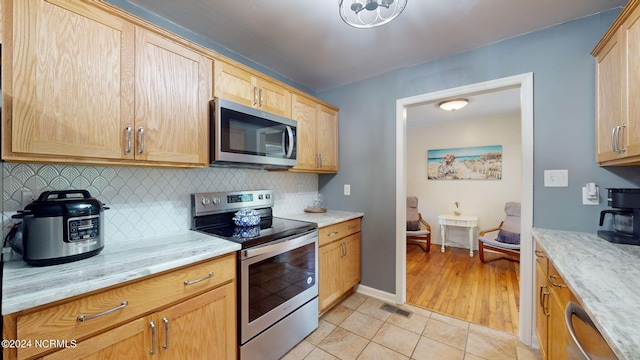 kitchen featuring light brown cabinets, light tile patterned floors, tasteful backsplash, stainless steel appliances, and light stone countertops