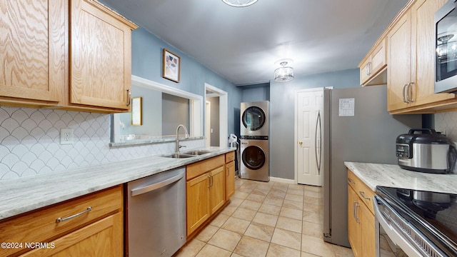 kitchen featuring light stone counters, sink, backsplash, stainless steel appliances, and stacked washer and dryer