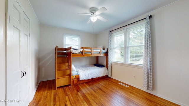 bedroom with multiple windows, wood-type flooring, crown molding, and ceiling fan