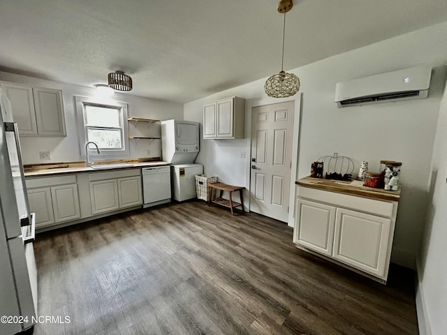 kitchen featuring a wall unit AC, freestanding refrigerator, a sink, dishwasher, and stacked washer / dryer