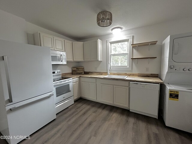 kitchen featuring hardwood / wood-style floors, white appliances, stacked washer / dryer, sink, and white cabinets