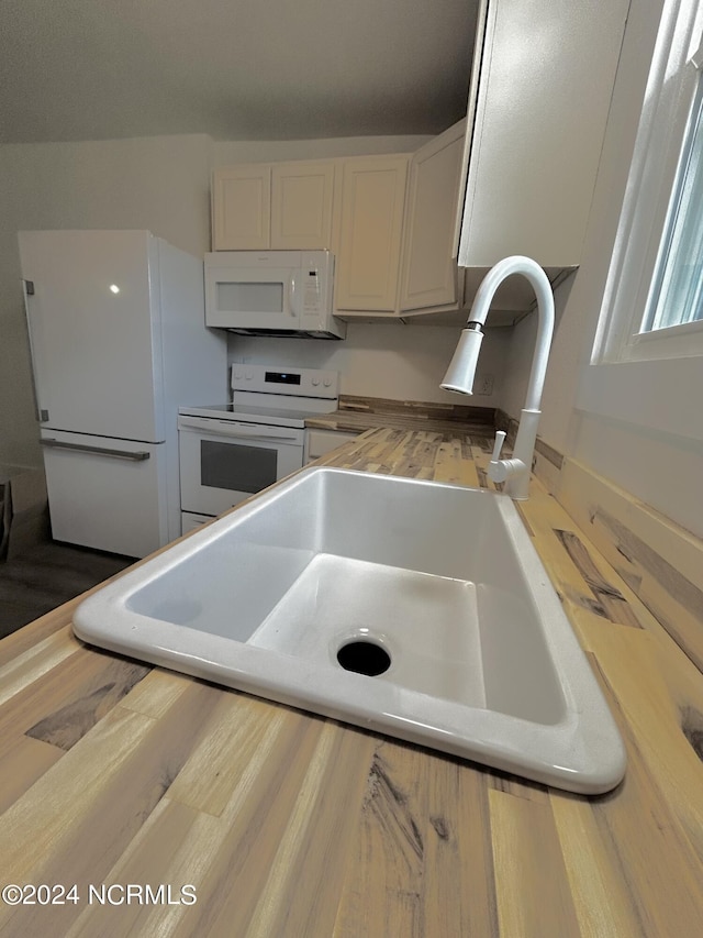 kitchen with white appliances, white cabinets, wood finished floors, and a sink