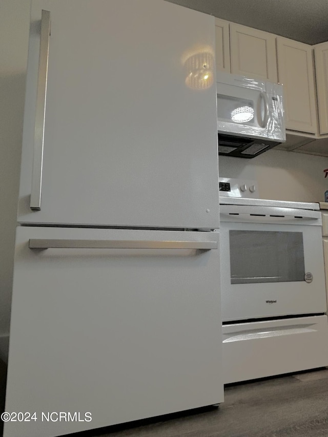 kitchen featuring white appliances, wood finished floors, and white cabinetry