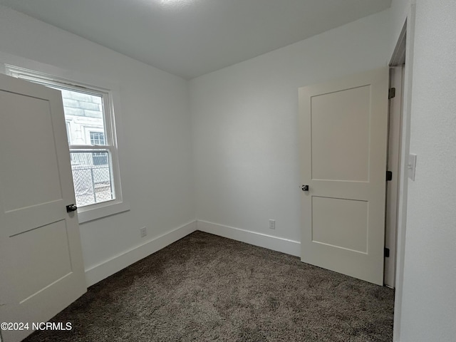 unfurnished room with baseboards and dark colored carpet