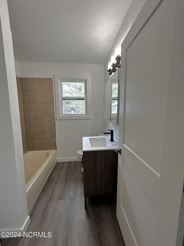 bathroom with a textured ceiling, vanity, a bathing tub, wood-type flooring, and toilet