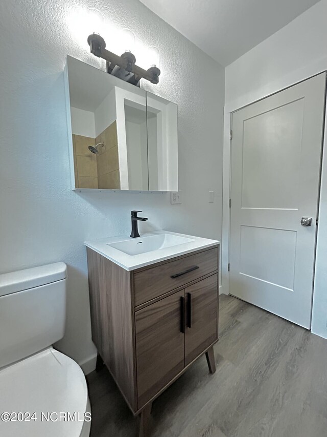 bathroom with hardwood / wood-style floors, toilet, a tile shower, and vanity