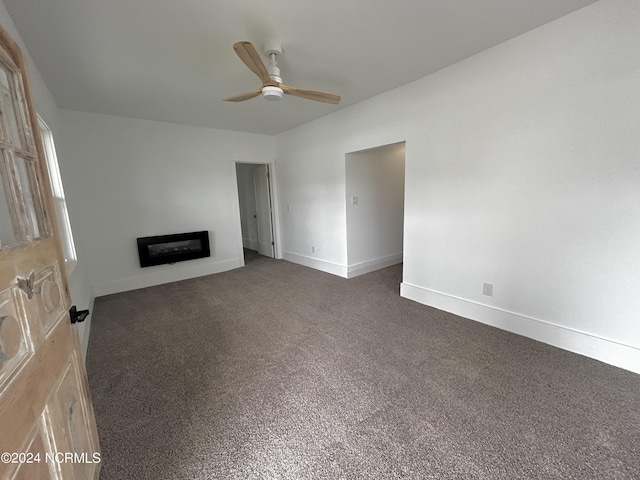 unfurnished living room with a glass covered fireplace, dark carpet, a ceiling fan, and baseboards