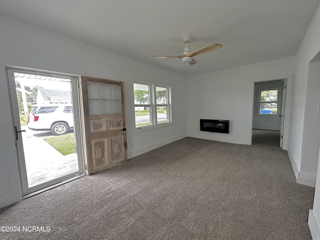 unfurnished living room featuring a glass covered fireplace, carpet flooring, baseboards, and ceiling fan