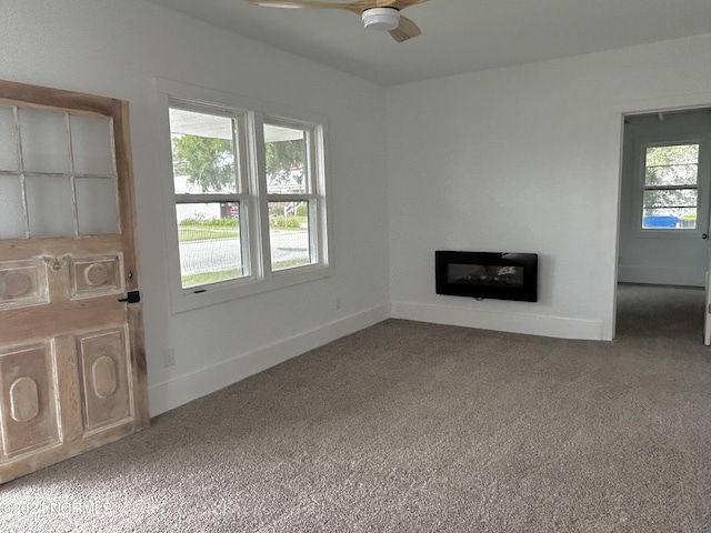 unfurnished living room with a glass covered fireplace, carpet, baseboards, and a ceiling fan