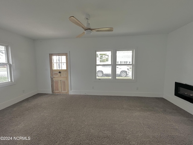 unfurnished living room featuring a glass covered fireplace, carpet flooring, a ceiling fan, and baseboards