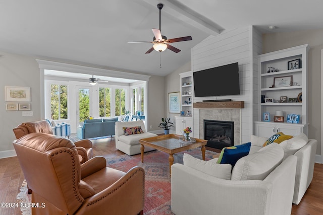 living room featuring ceiling fan, hardwood / wood-style floors, a tile fireplace, and vaulted ceiling with beams