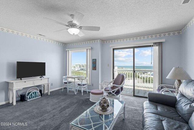 living room featuring dark colored carpet, a healthy amount of sunlight, a water view, and ceiling fan