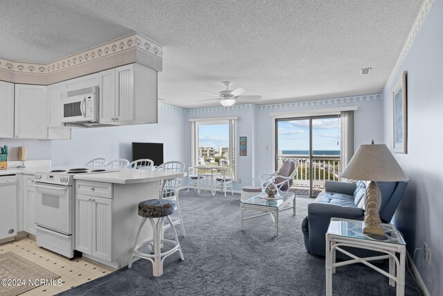 kitchen featuring kitchen peninsula, a kitchen bar, white cabinets, white appliances, and ceiling fan