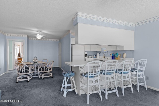 dining room with a textured ceiling, ceiling fan, sink, and dark colored carpet