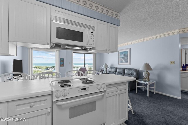 kitchen featuring white appliances, a textured ceiling, white cabinetry, and dark carpet