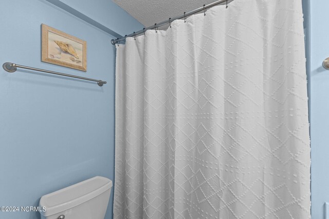 bathroom with toilet, a textured ceiling, and a shower with curtain