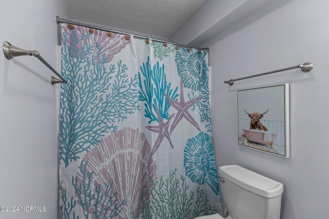 bathroom with toilet, a textured ceiling, and a shower with curtain