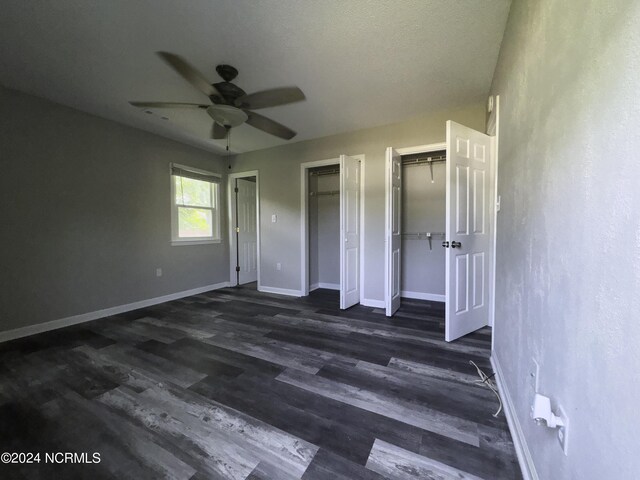 unfurnished bedroom featuring two closets, ceiling fan, and dark hardwood / wood-style floors