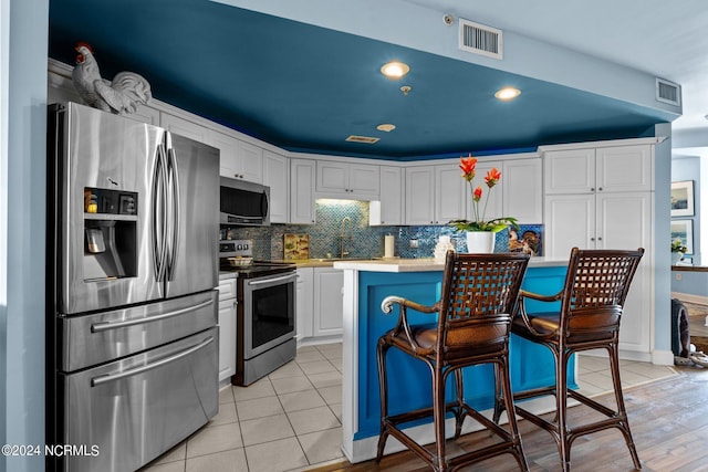 kitchen with visible vents, a sink, appliances with stainless steel finishes, white cabinets, and decorative backsplash