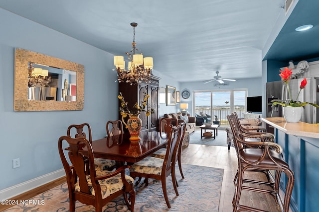 dining area featuring ceiling fan with notable chandelier, baseboards, and wood finished floors