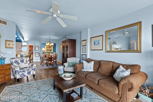 living room featuring ceiling fan with notable chandelier, visible vents, wood finished floors, and baseboards