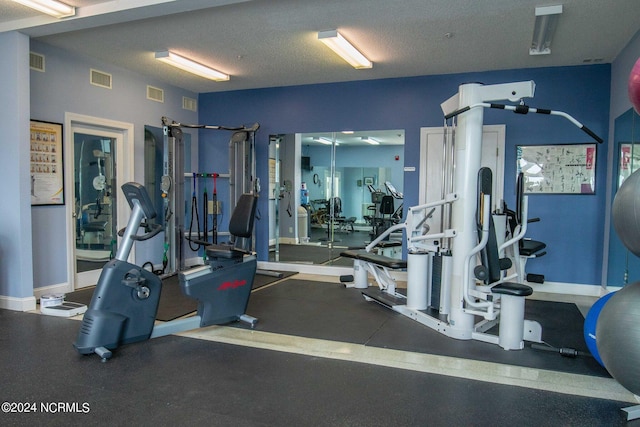 exercise room featuring visible vents, a textured ceiling, and baseboards