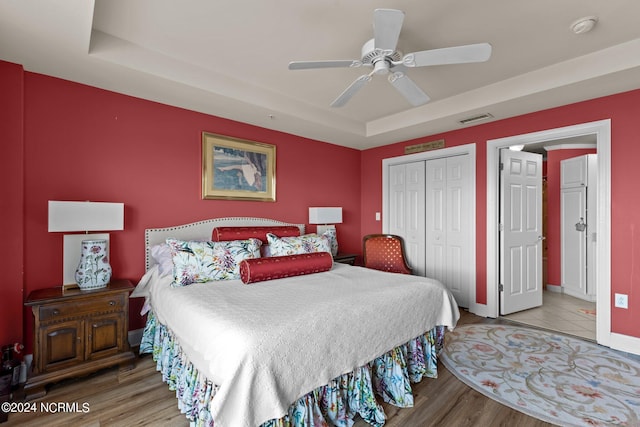 bedroom featuring a closet, hardwood / wood-style flooring, a raised ceiling, and ceiling fan