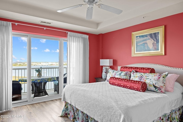 bedroom with access to exterior, visible vents, a water view, wood finished floors, and a ceiling fan