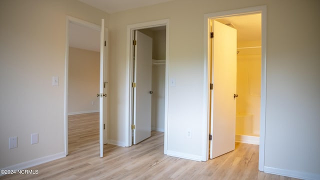 unfurnished bedroom featuring light wood-style floors, a closet, a spacious closet, and baseboards