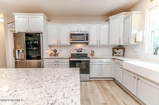 kitchen with light stone countertops, white cabinets, light hardwood / wood-style floors, and stainless steel appliances