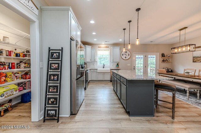 kitchen with white cabinetry, pendant lighting, light stone countertops, a kitchen breakfast bar, and a center island