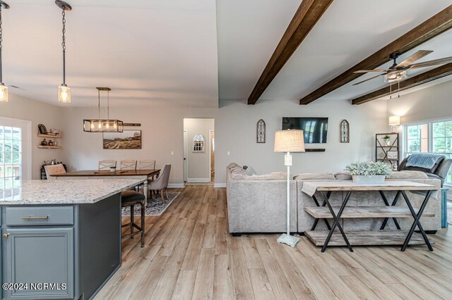 living room featuring beamed ceiling, light wood-type flooring, and ceiling fan with notable chandelier