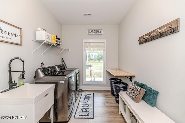 clothes washing area featuring washing machine and dryer, sink, and light wood-type flooring