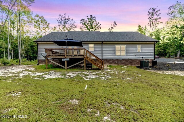 back house at dusk featuring cooling unit, a yard, and a deck