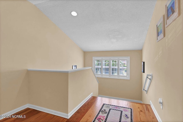 hallway with a textured ceiling, vaulted ceiling, and hardwood / wood-style flooring