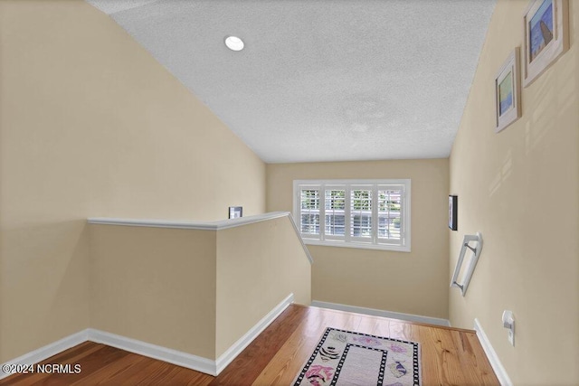 hall with an upstairs landing, a textured ceiling, baseboards, and wood finished floors