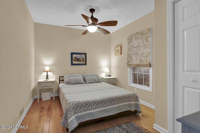 bedroom with a ceiling fan, light wood-type flooring, a textured ceiling, and baseboards