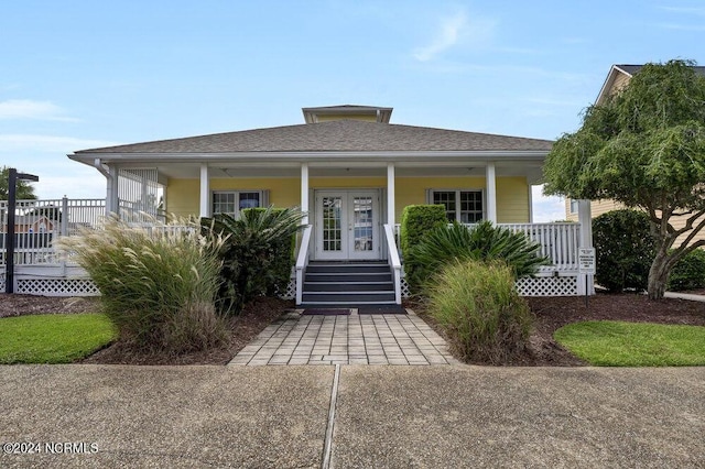 view of front facade featuring french doors, covered porch, and roof with shingles