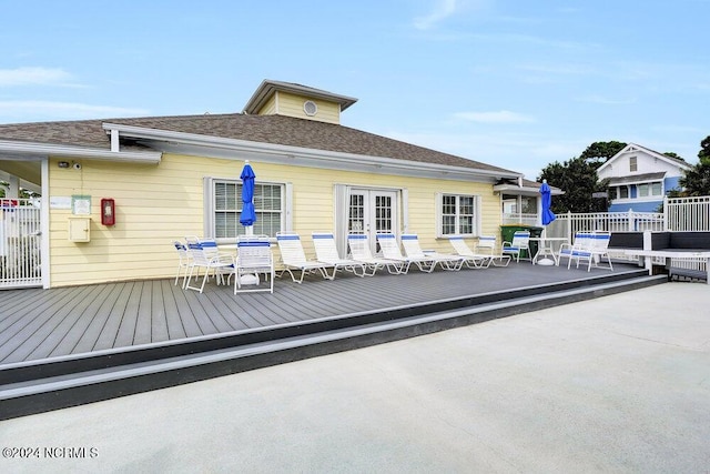 back of property with french doors, roof with shingles, a wooden deck, and fence