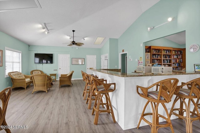 kitchen featuring ceiling fan, vaulted ceiling, wood finished floors, dark stone counters, and a kitchen bar