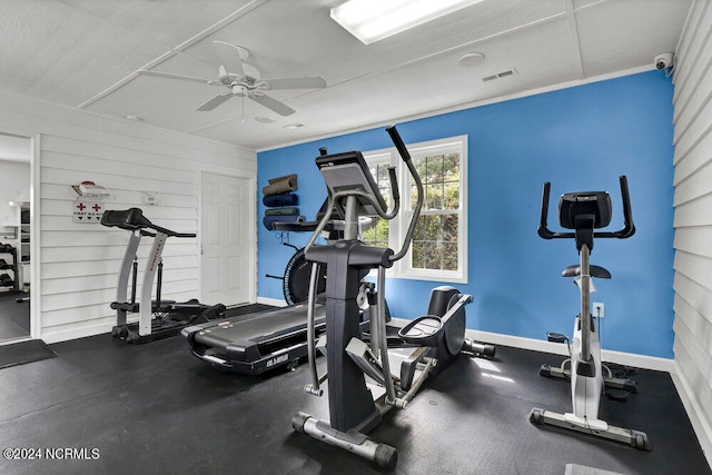 exercise room with ceiling fan and wood walls