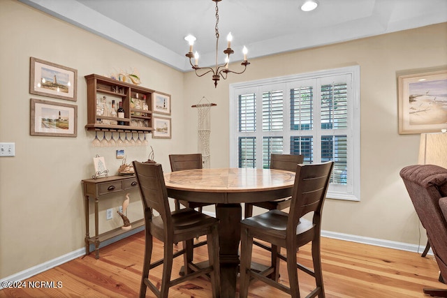 dining area featuring light wood-type flooring, a raised ceiling, and a notable chandelier