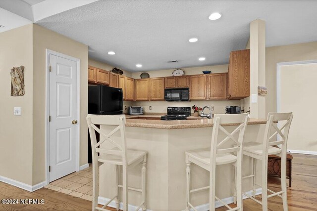 kitchen featuring black appliances, kitchen peninsula, light wood-type flooring, and a breakfast bar area