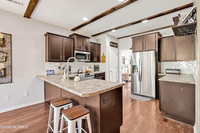 kitchen featuring light hardwood / wood-style flooring, stainless steel appliances, kitchen peninsula, and beam ceiling