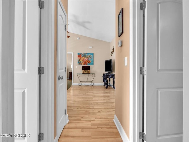 hall featuring baseboards, vaulted ceiling, and light wood finished floors